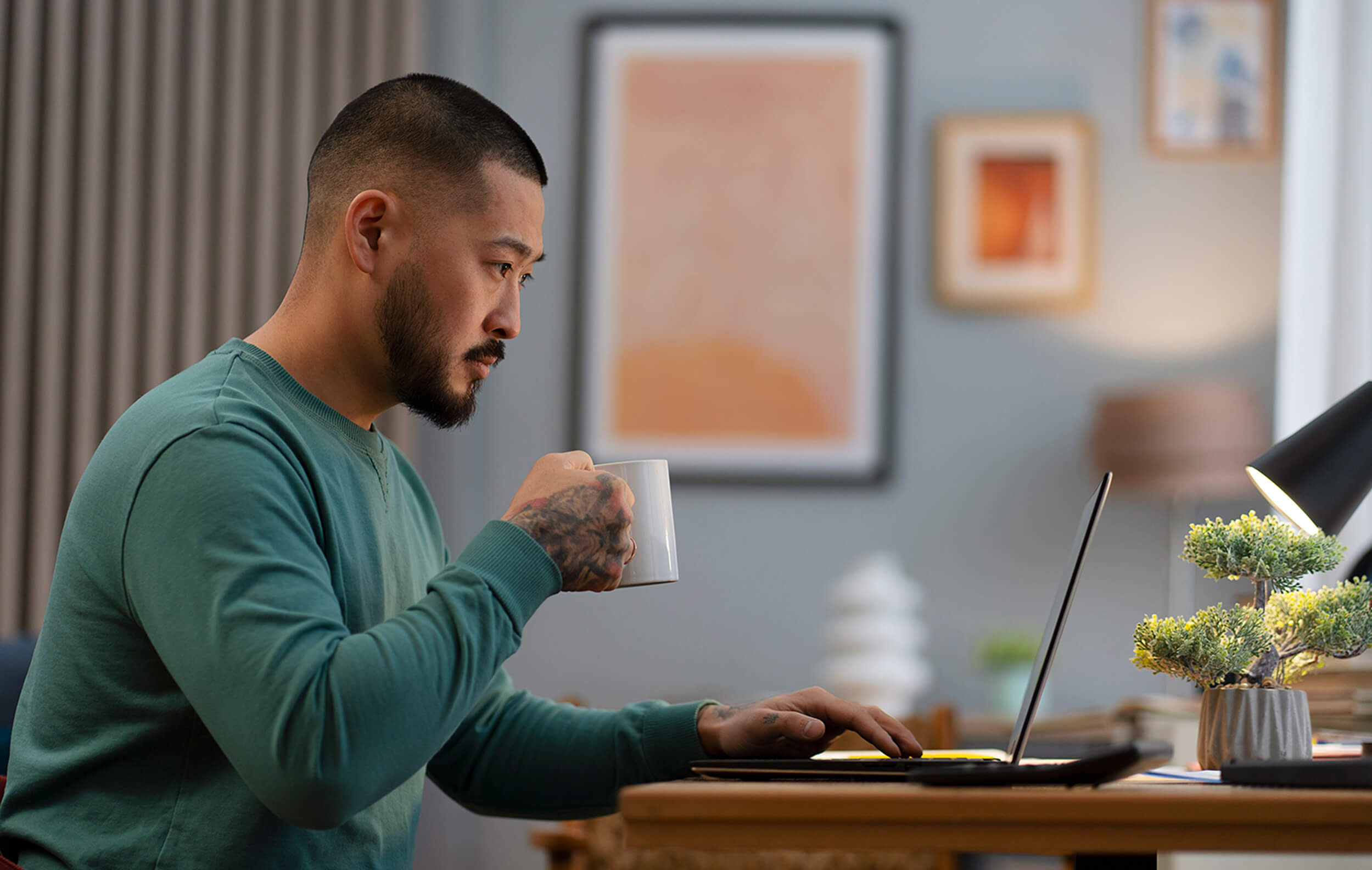 Male presenting older person holding mug and using laptop