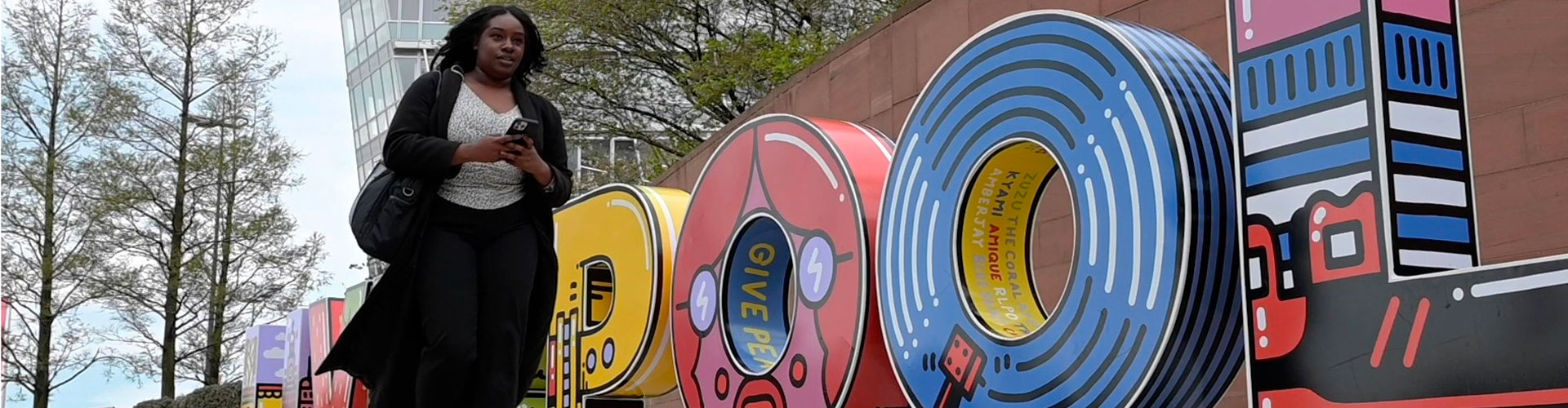 A woman walking in front of a Beatles themed 'Liverpool' sign