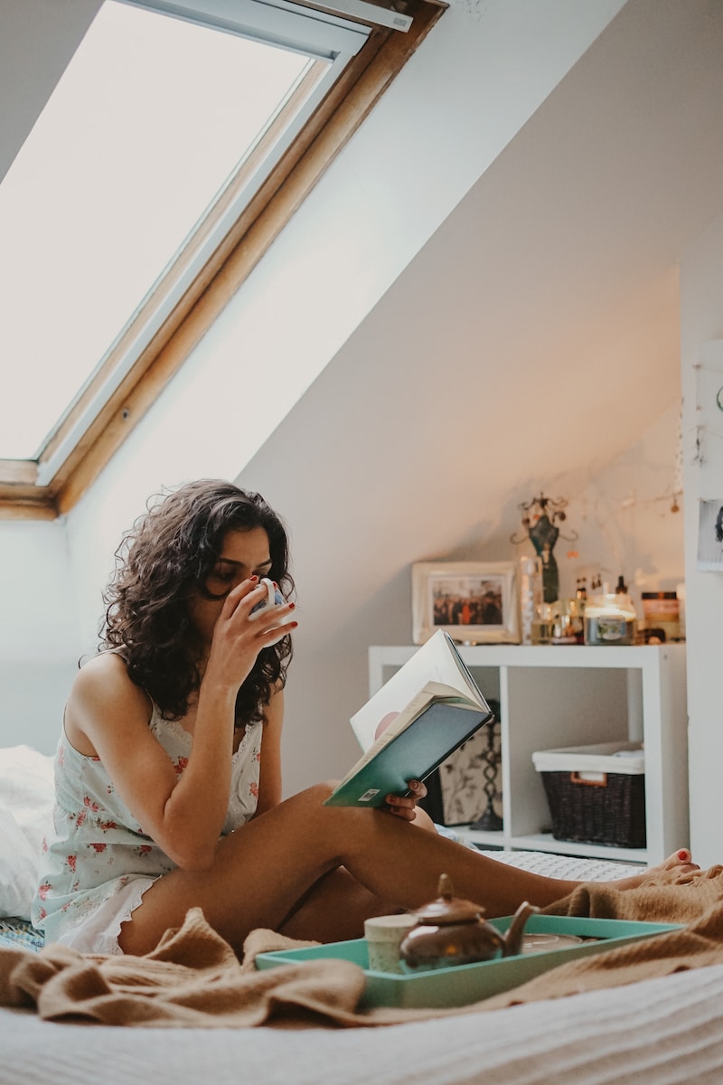 A girl sat on her bed unwell, reading a book.